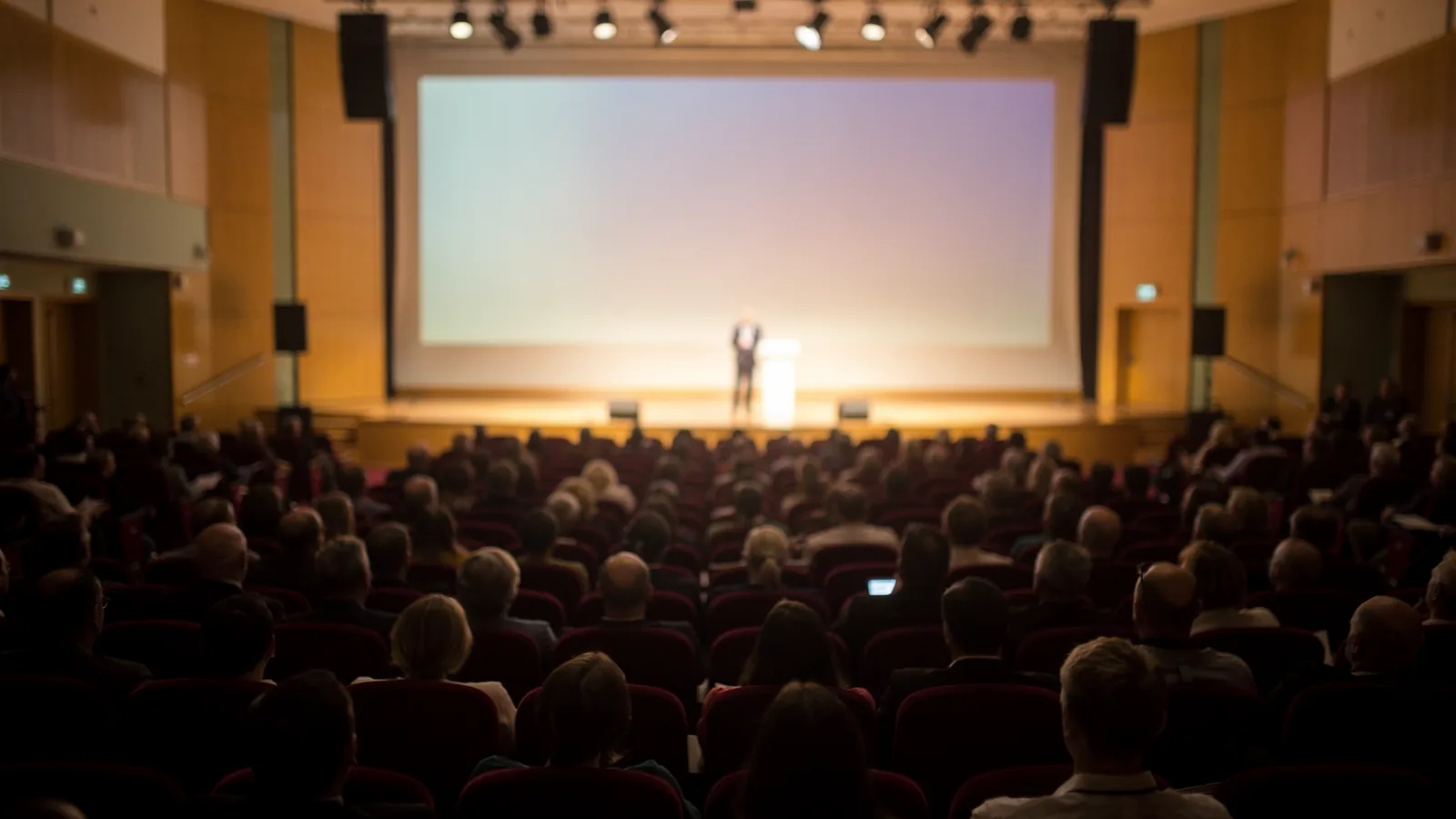 Widok z końca sali konferencyjnej na scenę i publiczność w trakcie wystąpienia
